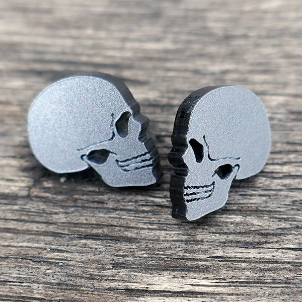 Stud earrings in the shape of a human skull in profile. Made from grey Perspex acrylic with a glitter finish.